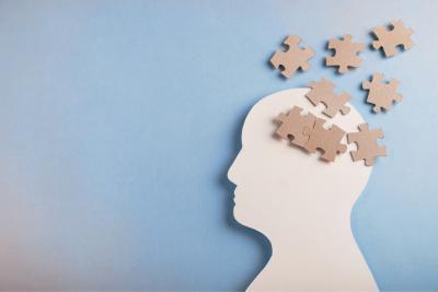 Papier uitgeknipt in de vorm van een hoofd, met puzzelstukjes erover verspreid ter hoogte van de hersenen