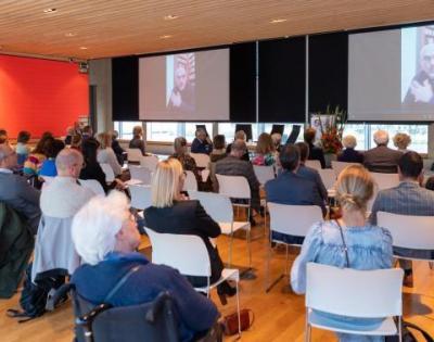 Publiek tijdens de academische zitting, met Prof. Dr. Bart Van Wijmeersch op het scherm