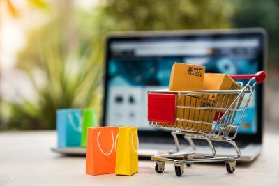 Miniwinkelkarretje met boodschappen en winkeltassen, met een laptop op de achtergrond